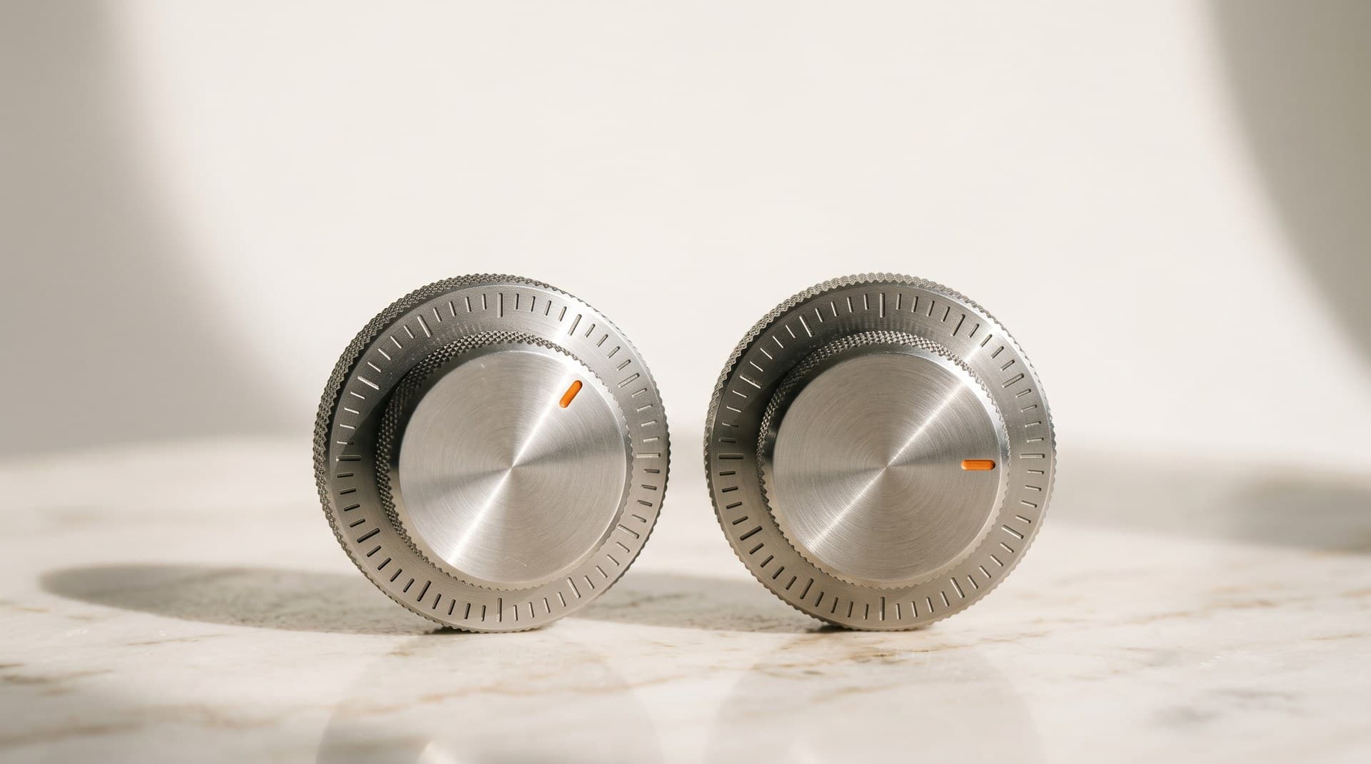 Two identical brushed steel rotary dials on a pale marble surface in bright daylight, the right dial's orange pointer turned one notch lower than the left, a metaphor for Claude Opus 5.5 shipping with a lower default effort level than Claude Opus 5