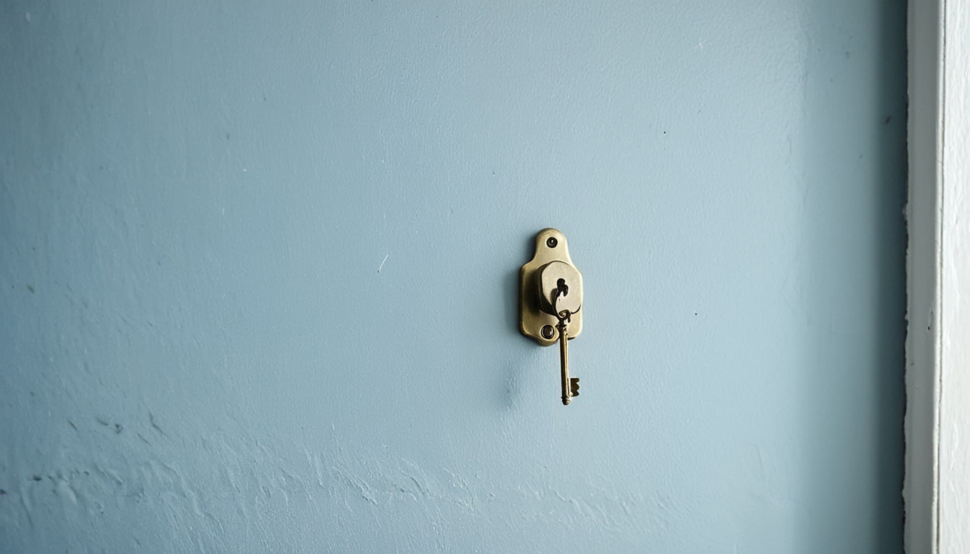 A single brass key hanging from one hook on an empty slate-blue wall, a visual for the Claude web fetch rule that only lets Claude fetch URLs someone already handed it