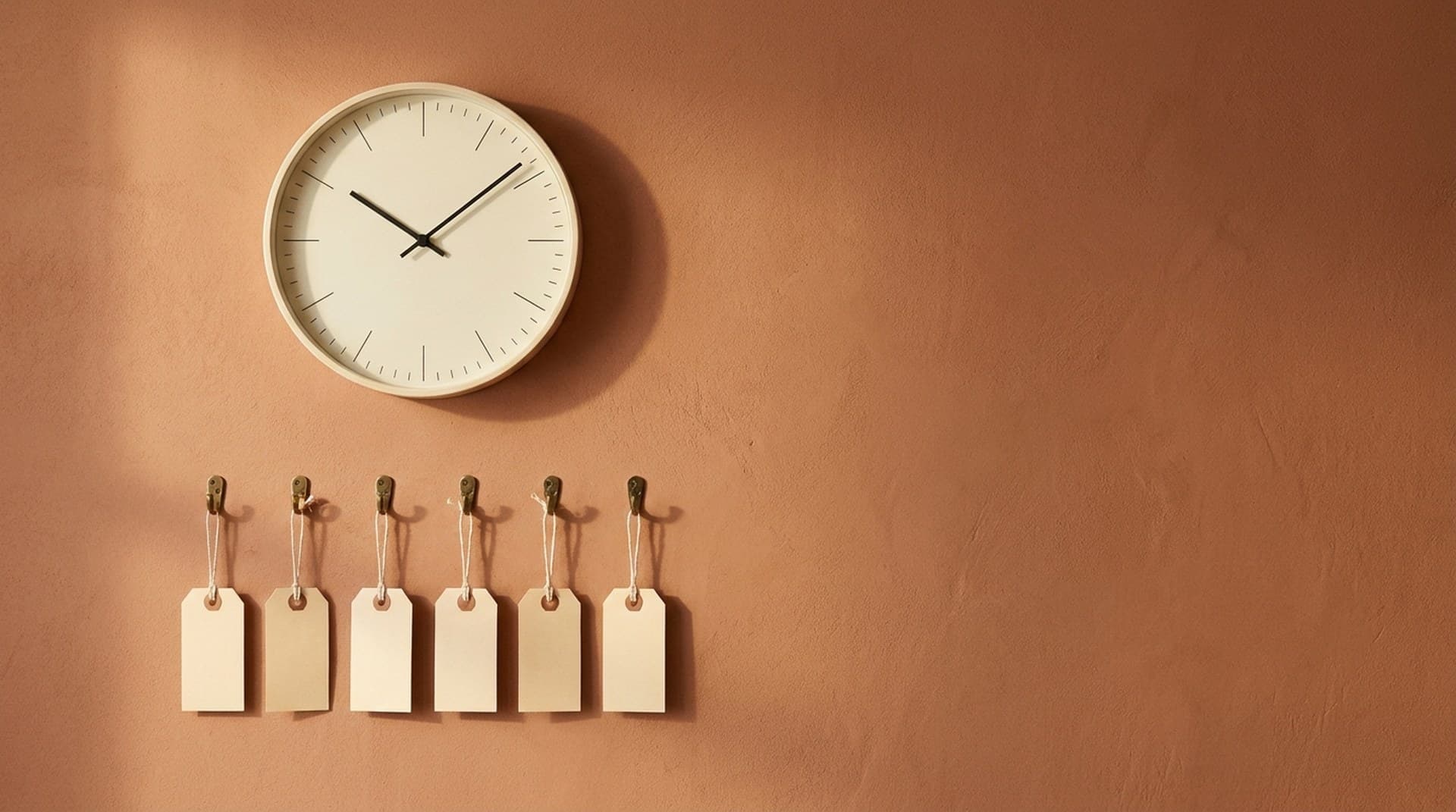 A minimalist wall clock above a row of blank manila tags on brass hooks, a visual for the n8n durable scheduler recording each Schedule Trigger run in advance