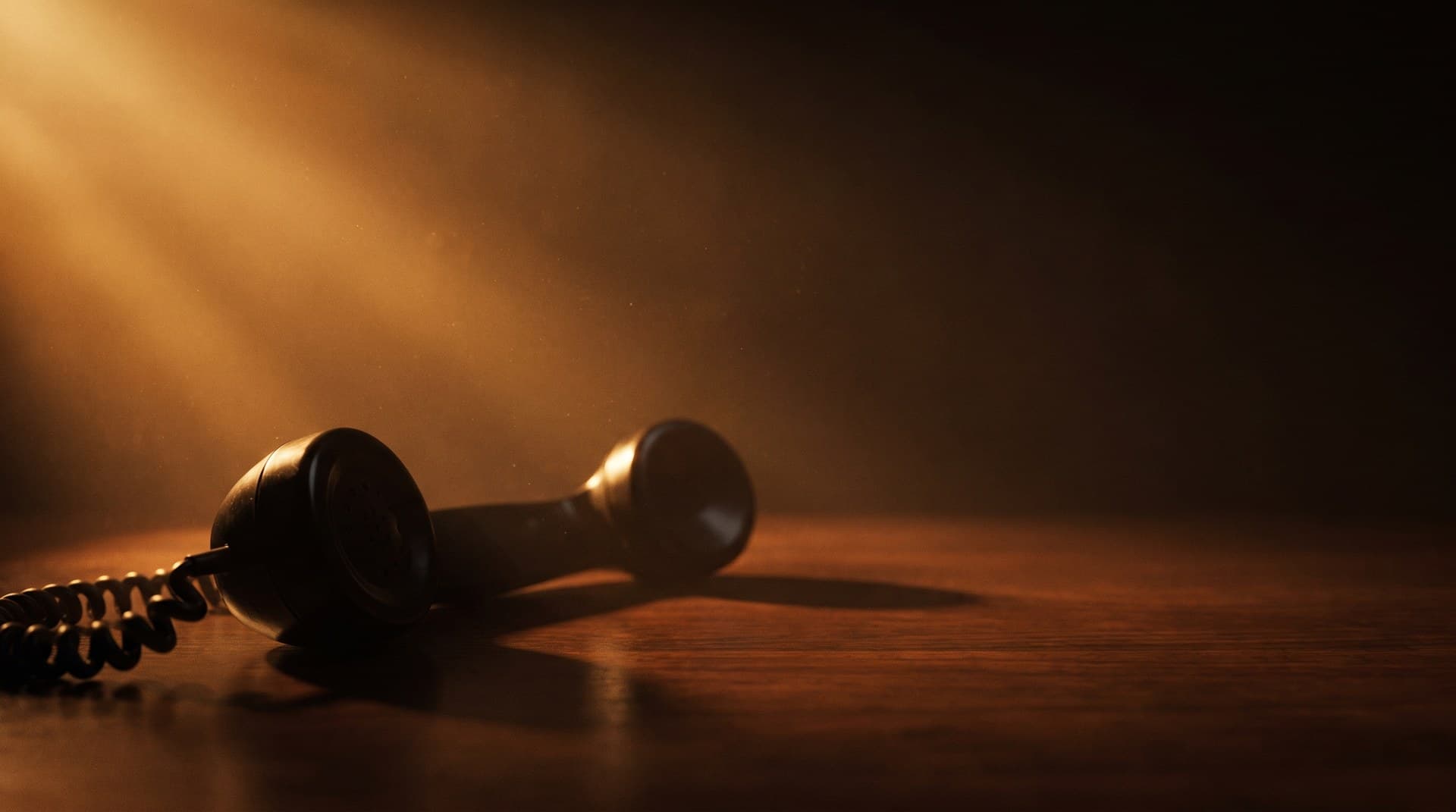 A classic black telephone handset lying off its cradle on a wooden desk under a warm amber light beam, representing a voice AI agent that cuts the caller off mid-sentence